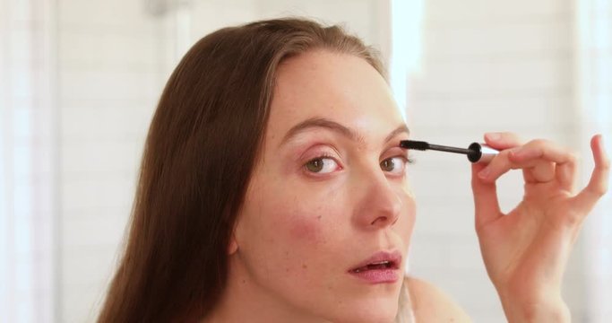 Pretty woman applying mascara eyelash in front of the mirror in bathroom