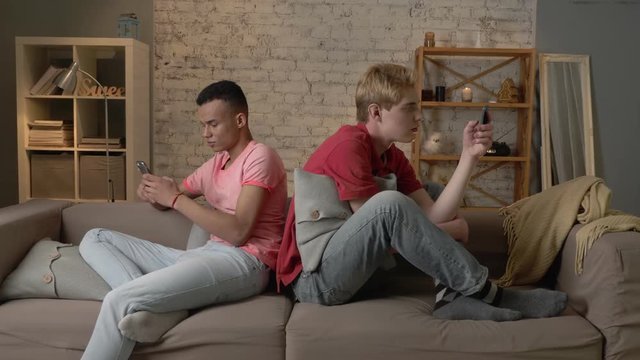 Two young mans are sitting on the couch and using a smartphones, gays, the problem of society, a new generation, lgbt lovers, homo, homosexuality concept 60 fps