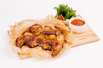 Grilled chicken Tabaka with sauce on a wooden plate on white background for menus.