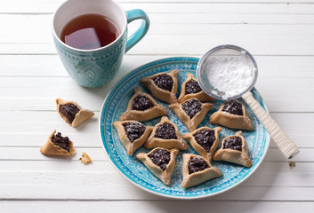 Traditional sweets for the Jewish holiday Purim. Hamantashen cookies or ears of Haman, triangular cookies with poppy seeds and raisins on a blue plate with a cup of tea, top view, free space