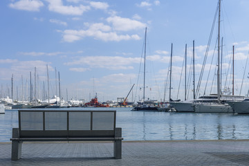 modern bench made of concrete and metal on the sea promenade at the backdrop of yachts and blue sky