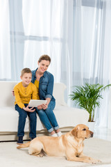 mother and son using tablet together with dog lying on floor on foreground