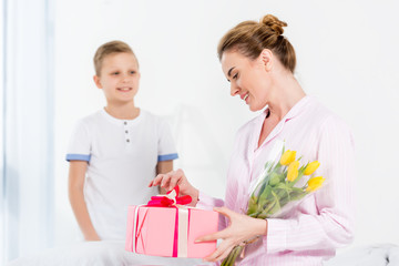 Obraz na płótnie Canvas son presenting gift and flowers for his beautiful happy mother on mothers day morning