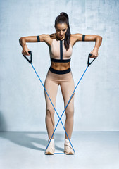 Fitness girl performs exercises with resistance band. Photo of fitness model workout on grey background. Strength and motivation