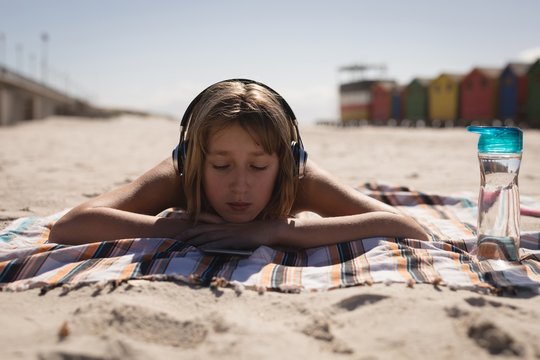 Teenage girl listening music on headphones while relaxing on the beach
