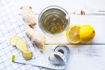 Healthy Breakfast, Sport, Fitness, Diet Concept. Tea for a weight loss with fresh lemon and ginger, white measure tape on a white wooden table with napkin, top view