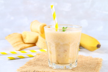 Banana smoothie with a paper tube and mint. Bananas are whole and cut on a gray background.