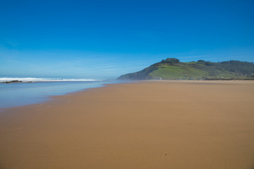 Fototapeta na wymiar beautiful landscape of Vega beach with vibrant colors: brown sand, green mountain, white waves in Cantabrian Sea and blue sky, in Ribadesella, Asturias, Spain, Europe 