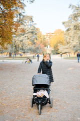 Young beautiful happy mother is walking in summer in a park with a baby in a stroller
