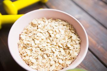 Healthy Breakfast, Sport, Fitness, Weight Loss, Diet Concept. Keeping fit with bowl of oatmeal and dumbbells, dark wooden background