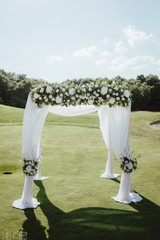Beautiful wedding archway in the green field. Arch decorated with white cloth and flowers.