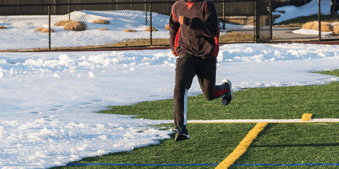 Runner on green turf field with snow on it