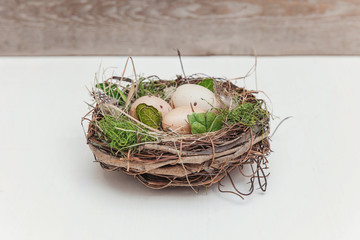 Obraz premium Easter decoration with egg in nest with moss on rustic white wooden background. Easter concept. Flat lay top view copy space. Spring greeting card