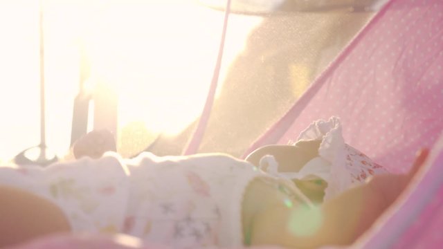 Little baby in bonnet lying in pink bassinet outdoor. Shot of child in bright warm sunlight