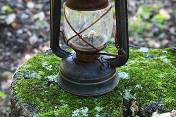 Old Rusty camping Lantern on a mossy tree stump