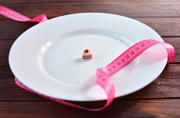Tape measure and little sweeet cake on a white big plate, as a concept of health care and diet.