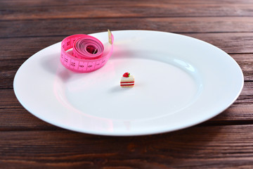 Tape measure and little sweeet cake on a white big plate, as a concept of health care and diet.