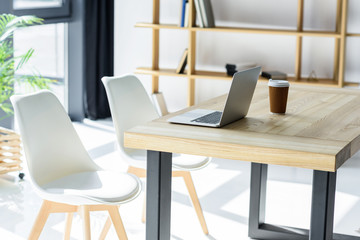 Laptop and coffe cup on table in modern office