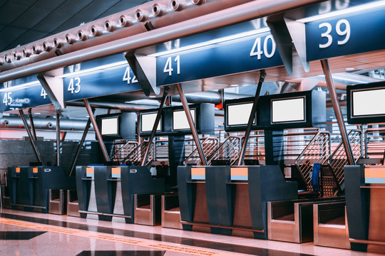 Interior of check-in area in modern airport: luggage accept terminals with baggage handling belt conveyor systems, multiple blank white information LCD screen templates, indexed check-in desks