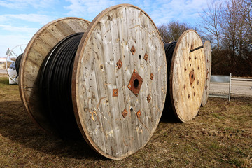 Two wooden coils with electric black cables outdoors in a field under a blue sky