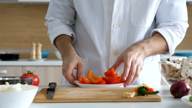 Male cook comes from the back of the kitchen and placing sweet red papper in a plate