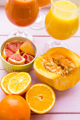 Healthy Food, Diet Concept. Two glasses of fruit and vegetable smoothie with pieces of fresh orange, pumpkin and grapefruit on pink wooden background
