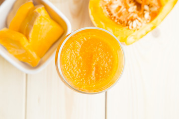 Fototapeta na wymiar Fruit and Vegetable Smoothie, Healthy Food, Diet Concept. A glass of smoothie with a piece of pumpkin and cut mango in a bowl on a light wooden background, top view