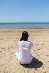 Lonely brunette woman with lobg hair on a beach and looking on sea. Back view.