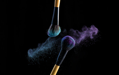 Two make up brushes with powder explosion dust in blue and purple color, close up