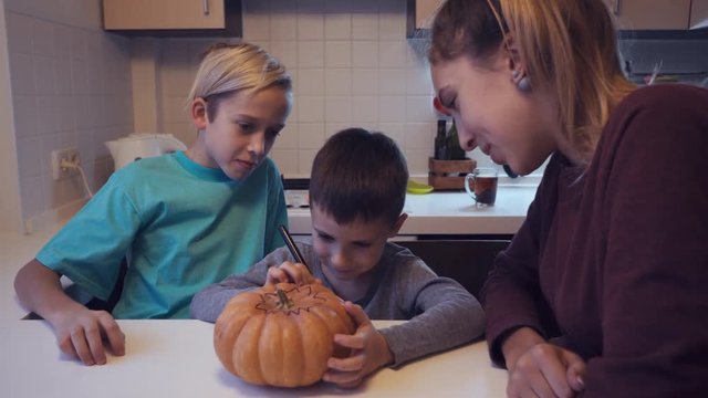 Elder children looking their small brother drawing on pumpkin