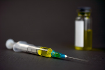 syringe with a yellow drug lies on a gray dark background, defocused glass jar of the drug, concept of drug addiction, treatment of serious diseases. selective focus, close-up,  copy-space