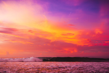 Naklejka na ściany i meble Waves in ocean at bright pink sunset or sunrise. Ocean with warm sunset colors
