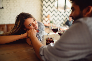 Romantic couple sitting in cafe and drinking wine. Attractive girl holding her boyfriend hand and looking at him.