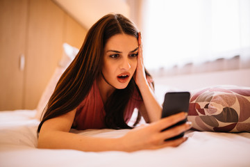 Obraz premium Surprised girl lying on bed at using mobile.