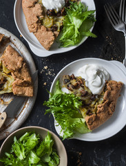Rustic vegetarian wild mushrooms and potatoes whole grain pie with greek yogurt and green salad on a dark background, top view. Flat lay