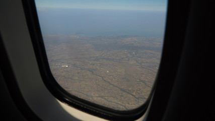 Fototapeta premium View through an airplane window on the tropical island, ocean, sky and clouds. Aerial view sea, clouds and sky as seen through window of an aircraft. Travel concept.