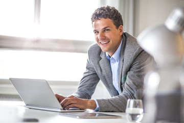 Portrait of smiling young businessman using laptop in office