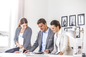 Happy young business people discussing over brochure at office desk