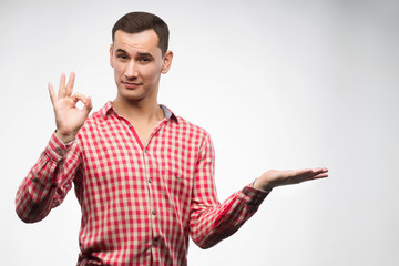 Fototapeta premium Young man wearing checkered red shirt Holds a copy space on his hand and shows a sign ok