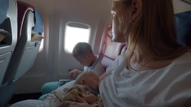 Woman with two kids traveling by air. Elder son playing game on digital tablet while mother breastfeeding baby
