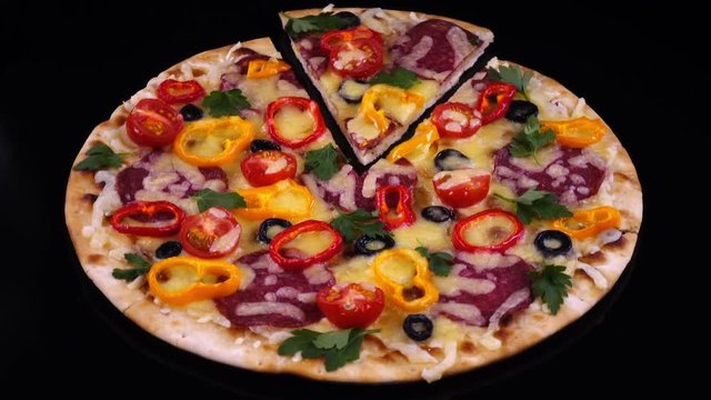 Homemade tasty pizza with cut off piece rotates on black background in 4K.
