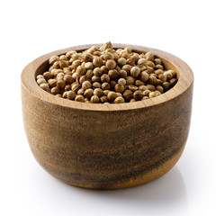 Whole dried coriander seeds in dark wood bowl isolated on white.