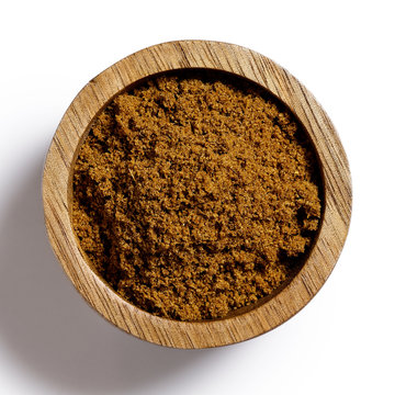 Ground cumin in dark wood bowl isolated on white from above.