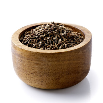 Dry caraway or cumin seeds in dark wood bowl isolated on white.