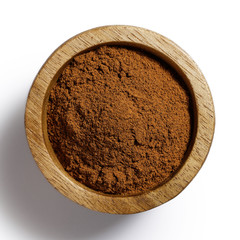 Finely ground cinnamon in dark wood bowl isolated on white from above.