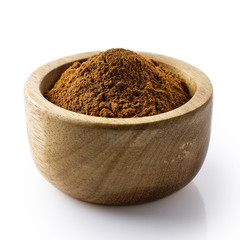 Finely ground cinnamon in dark wood bowl isolated on white.