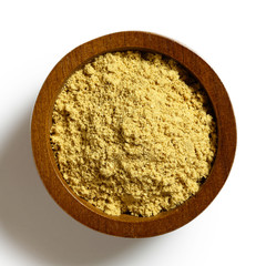 Finely ground dry ginger in dark wood bowl isolated on white from above.