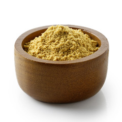 Finely ground dry ginger in dark wood bowl isolated on white.