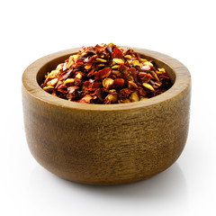 Coarsely ground chilli peppers in dark wood bowl isolated on white.