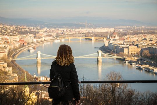 Young woman is looking at the Chain bridge, Budapest parliament and cityscape from The Citadella which is a fortification located upon the top of Gellert Hill in Budapest, Hungary.
